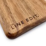 A wooden serving board with a smooth acacia finish featuring a branding logo.