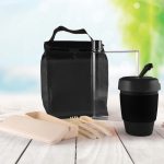 A black picnic bag contains a drink bottle, a takeout container, utensils, and a black reusable cup.