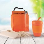 An orange picnic pack containing a drink bottle, reusable cup, utensils, and food containers, all in a vibrant setting.