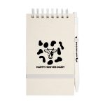 A spiral notepad with a tan cover and a pen, featuring a logo and a cow pattern design.