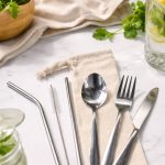 A stainless steel cutlery and straw set in a calico pouch, featuring a spoon, fork, knife, and two straws.