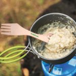 A cooking pot containing a creamy mixture with a green handle and a wooden fork labeled "freshfood" resting inside it.
