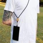 A phone lanyard featuring a black strap and wooden bead, securely holding a smartphone on a person's back.