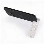 A white phone stand supports a black smartphone, featuring two circular grips for stability.