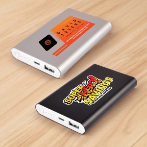 Two power banks displayed on a wooden surface: one silver with an orange label, and one black with a colorful logo.