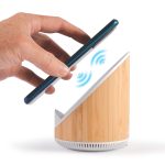 A wireless charger and speaker with a bamboo design, showing a hand placing a phone atop the device.
