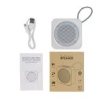 A white wireless speaker with a round mesh speaker area, USB cable, instruction manual, and brown packaging.