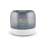A compact speaker featuring a grey translucent cover and a white base, with branding on the front.