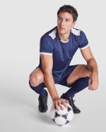 A man in a navy blue sports uniform with white accents, crouching and holding a soccer ball.