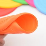 An orange silicone flyer with a smooth, flexible surface, surrounded by various brightly coloured flyers.