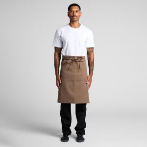 A man wears a brown canvas half apron over a white t-shirt and black pants, with a tied waist and a logo.