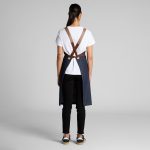 A denim apron with brown straps, worn by a person facing away, paired with a white t-shirt and black trousers.