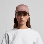 A light brown cap with a flat brim and a logo, worn by a woman in a white t-shirt.