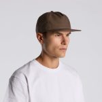 A man wearing a brown cap, facing slightly to the right. The cap has a simple design and a straight brim.