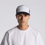 A two-tone trucker cap in white and black, featuring a logo on the front, worn by a model in a white t-shirt.