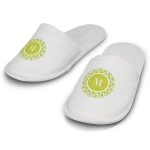 White waffle slippers with a green circular design and a logo on the front. Soft, textured fabric with a cushioned sole.