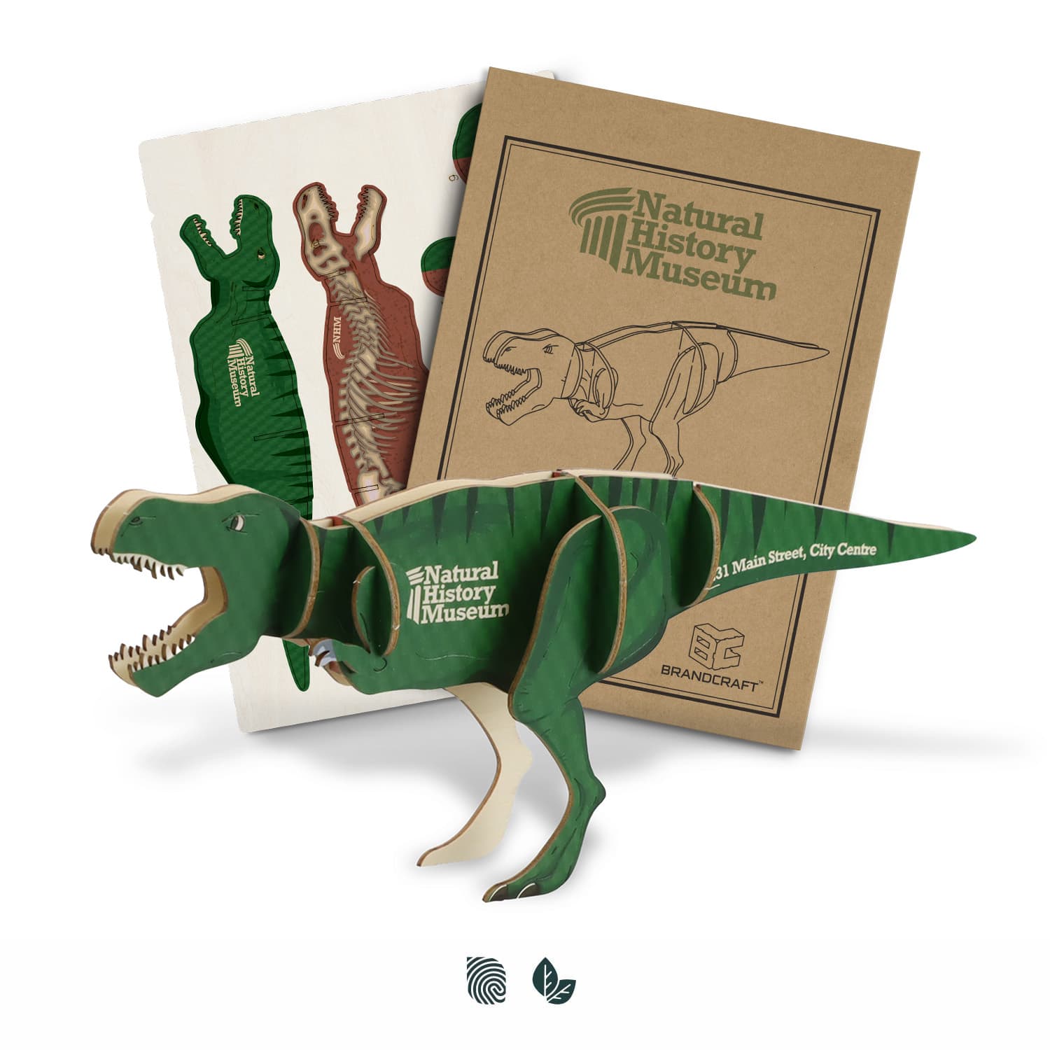A green wooden Tyrannosaurus Rex model next to instructional sheets, featuring a logo on the packaging. BRANDCRAFT Tyrannosaurus Rex Wooden Model - Image 1