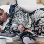 A decorative blanket featuring vibrant floral patterns in various colours, draped over a person lounging on a couch.