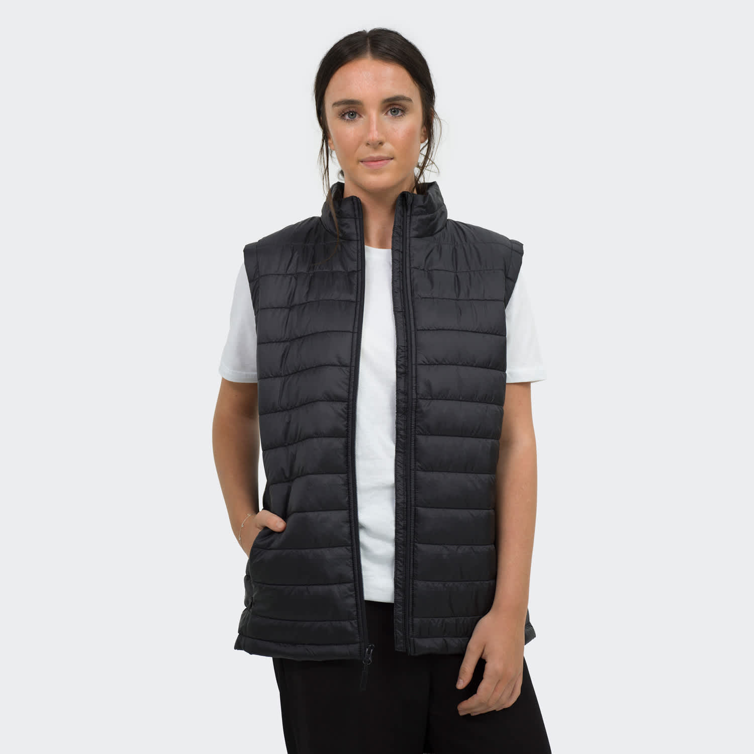 A woman is wearing a black puffer vest over a white t-shirt, featuring a logo and zip-up design. TRENDSWEAR Frazer Womens Puffer Vest - Image 1