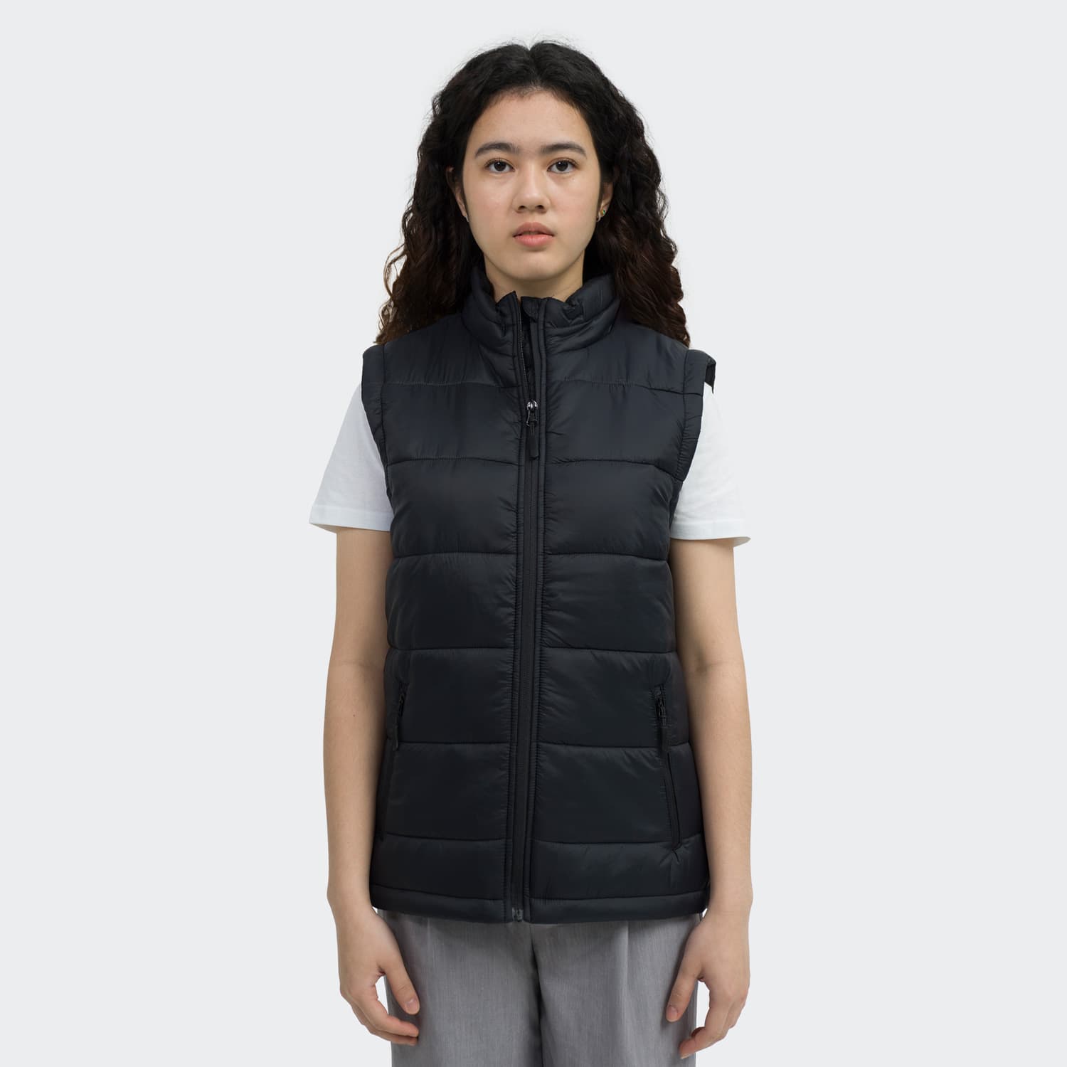 A woman models a black puffer vest with a front zip and a high collar, featuring a logo. TRENDSWEAR Milford Womens Puffer Vest - Image 1