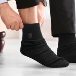 Black socks being worn, featuring a subtle logo on the side. The person is adjusting them while seated.