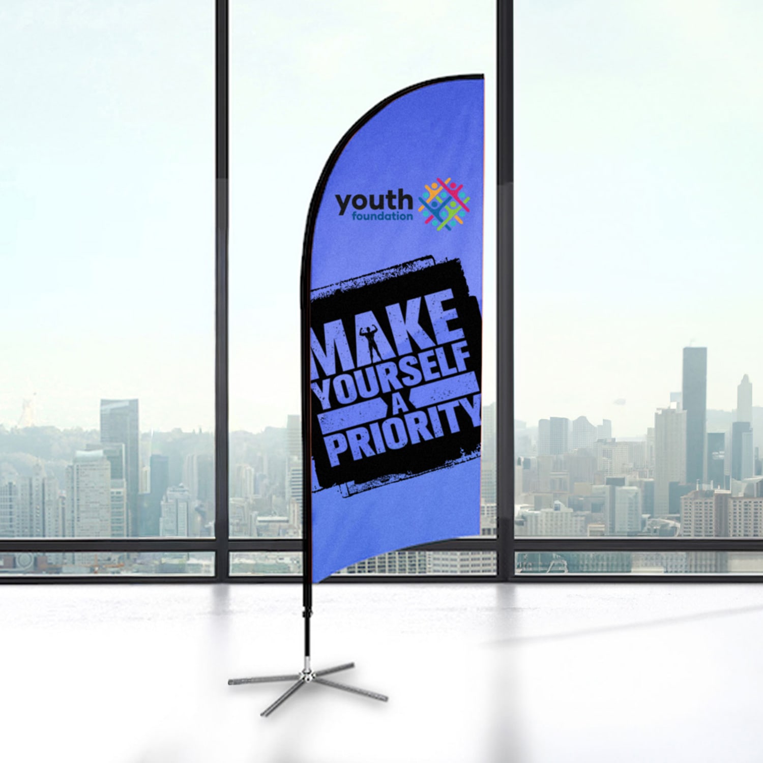 A small feather flag kit featuring a blue background and a logo, displayed indoors with a city skyline view. Small Feather Flag Kit - Image 1