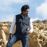 A man is wearing a navy Jandro Vest over a white long-sleeve shirt, posed against a rocky landscape.