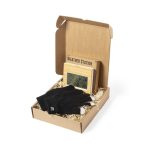 A gift box containing a wooden weather station and black gloves, nestled in straw filler.