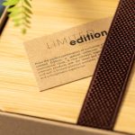 A brown woven strap rests on a wooden surface, accompanied by a card detailing a limited edition product.