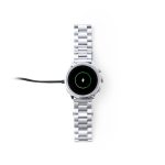 A silver smartwatch with a metal band and a charging cable attached. The watch has a circular display.