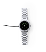 A silver smart watch with a round face and a charging cable attached. The watch features a sleek stainless steel band.