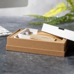 A beige box partially opened, revealing a white wireless charger inside, set against a grey surface and greenery.