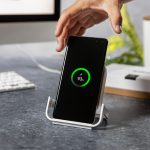 A wireless charger in white, holding a smartphone displaying a charging indicator.
