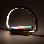A wireless charger lamp with a wooden base and a glowing white arch, holding a smartphone.