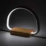 A modern lamp with a curved light encased in a white material and a wooden base. Features a sleek design.