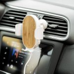 A wireless charger holder with a bamboo finish, mounted on a car air vent, next to a car display screen.