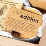A white charger holder with a natural wood base, accompanied by a brown card featuring information about a limited edition.