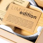A wireless charger holder in white, featuring a logo, nestled in a cardboard package with a limited edition card.