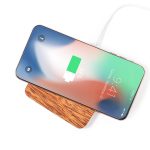 A wireless charger with a wooden base and a smartphone displaying a battery charge indicator.