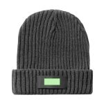 A grey beanie hat with a ribbed texture and a dark rectangular patch. It features a logo or branding.