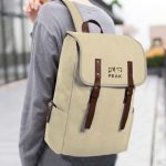 A beige backpack with brown straps and a logo, being worn on a person’s back outdoors.