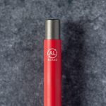 A red metal pen featuring a grey metal tip and an emblem indicating it is made from recycled materials.