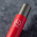 A red metal pen with a black tip and a logo indicating it is made of recycled materials.