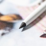 A white stylus pen with a pointed black tip rests on a colourful printed surface. It features a logo.