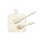 A cream pot holder with a spatula and basting brush in off-white. The set features a textured grip and has branding.