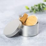 A silver tin container holds a wooden USB and a circular wooden item, with greenery in the background.