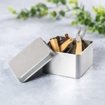 A silver gift box containing a multi-tool with wooden handles and pliers, set against a soft grey background.