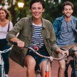 A group of people riding bicycles in a park, featuring a woman smiling while cycling.