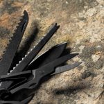 A multifunction pocket knife with black tools, including scissors and various blades, displayed on a textured surface.