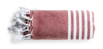 A rolled Vedant Towel Pareo in a reddish hue with white stripes and tassels on one end. It features a logo.